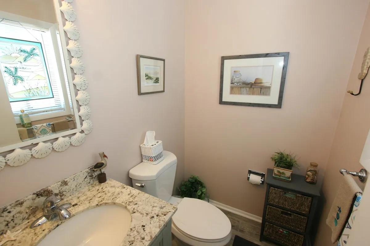 A calming bathroom scene with a shell-framed mirror, granite countertop, decorative wall art, a small plant, and woven storage basket. The space feels fresh and inviting, ideal for moments of relaxation and personal care.
