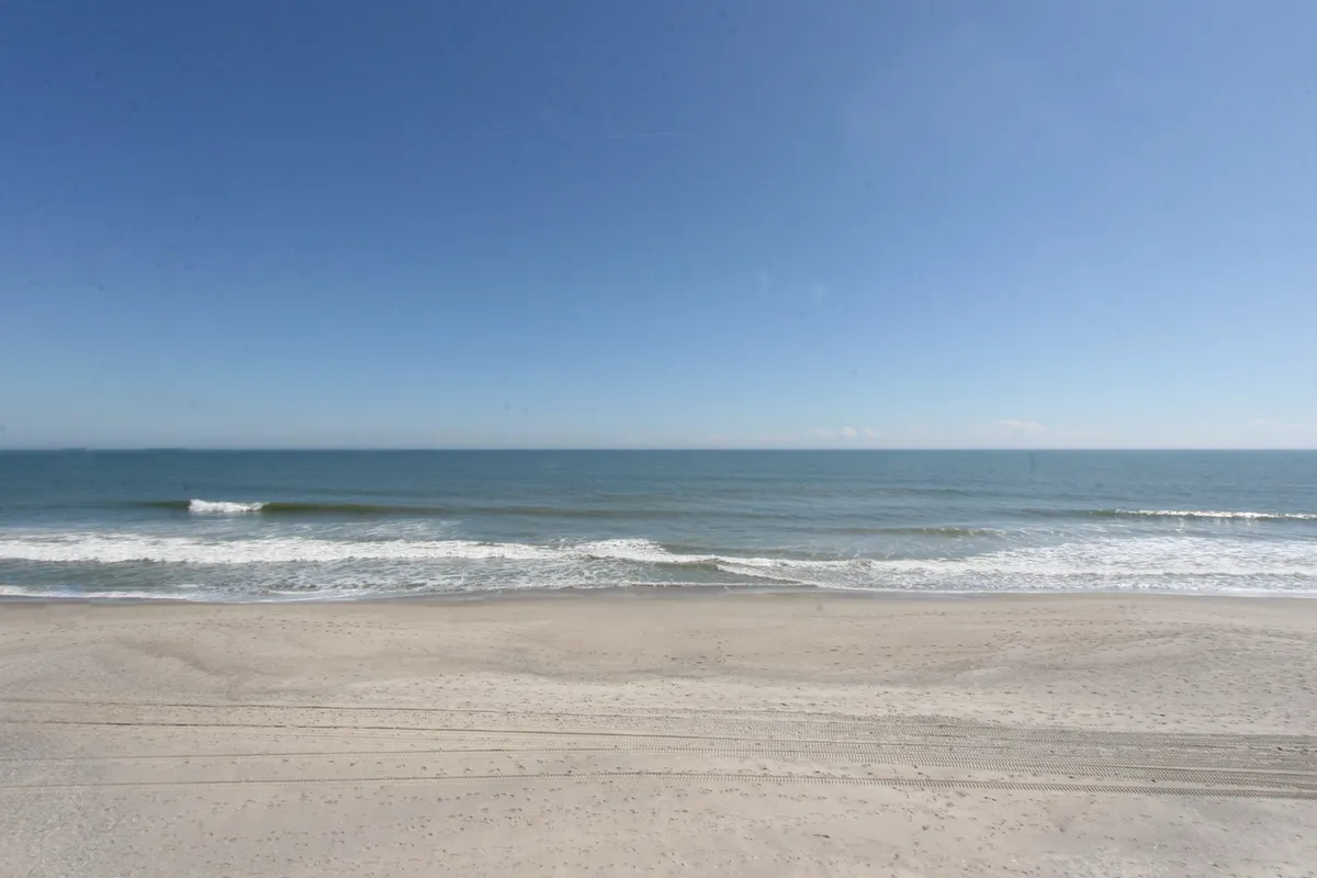 A sweeping view of the ocean, sandy shoreline, and expansive sky. The image captures the tranquility of undeveloped beachfront, inviting peaceful strolls, sunrise watching, and beachcombing along the water's edge.