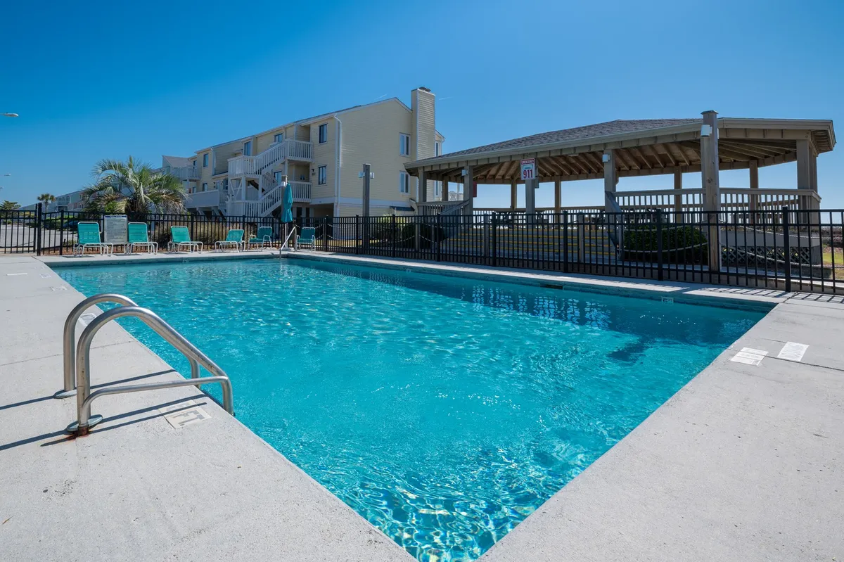 A relaxed poolside scene with a swimming pool surrounded by lounge chairs, a gazebo, and lush landscaping. The space invites sunbathing, socializing, and enjoying sunset views or morning swims.