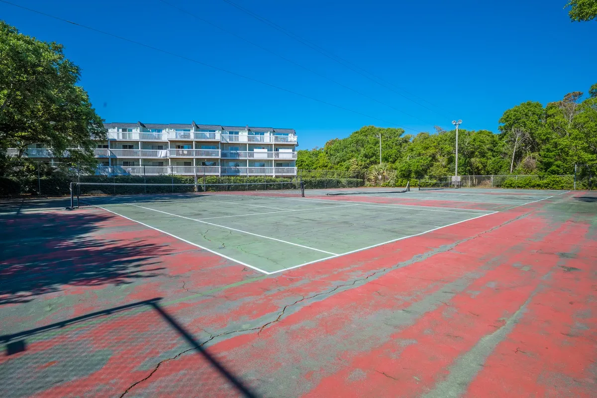 A well-maintained tennis court nestled among lush greenery, with residential buildings visible in the background. The space invites energetic play and community connections.