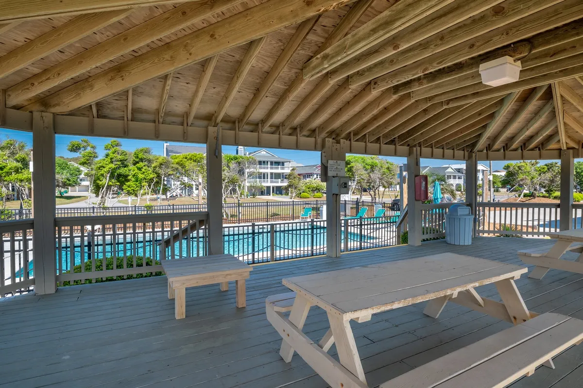 An open-air structure with wooden picnic tables, glimpses of the resort pool, and a casual, friendly vibe. The space is designed for outdoor family gatherings, picnics, and playful moments near the pool, capturing the spirit of communal fun.