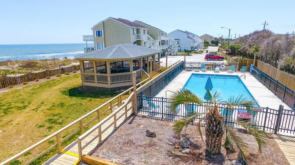 An inviting outdoor pool with a gazebo, palm tree, and a stunning ocean view in the background. Lounge chairs surround the pool, and the mood is bright and leisurely, perfect for sunny days spent swimming and socializing.