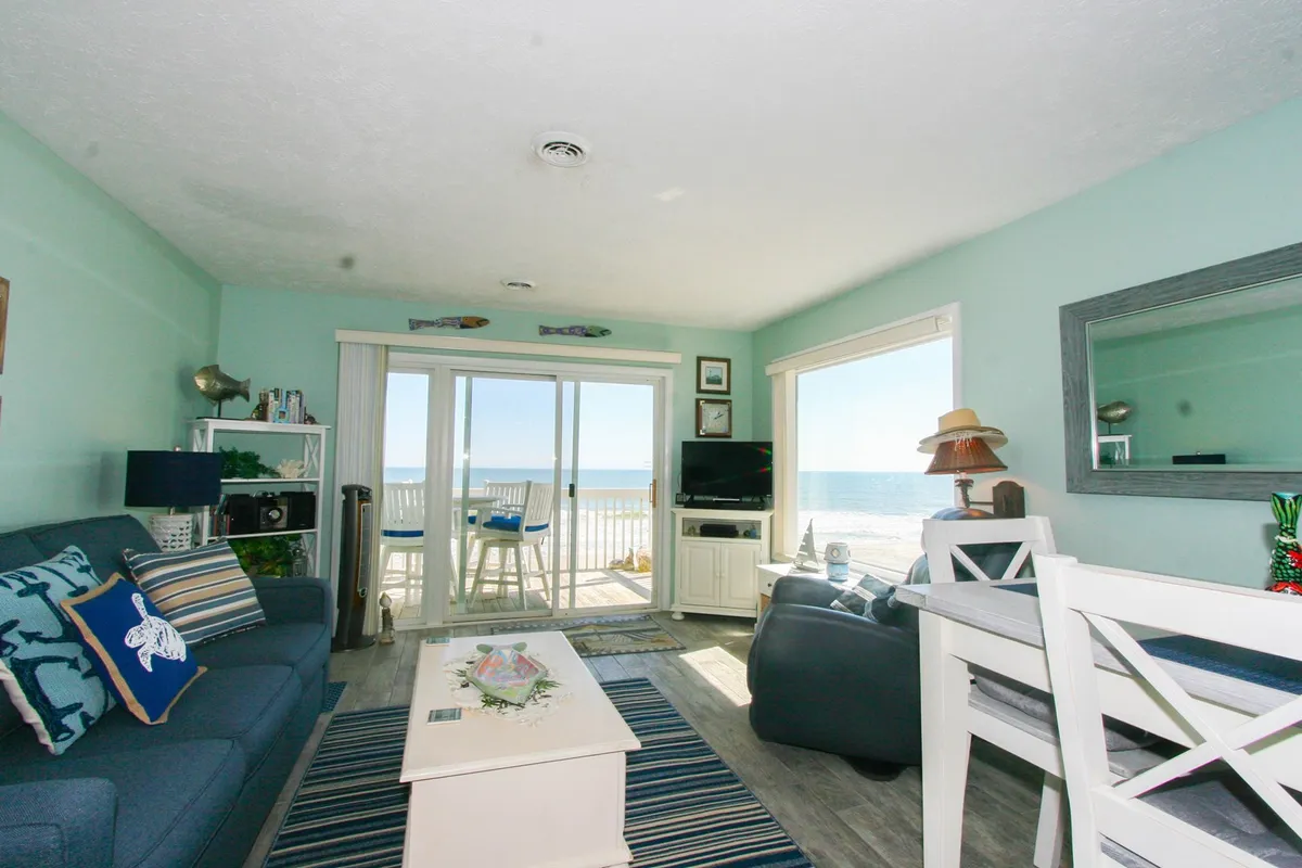 A tranquil living/dining space with a sofa adorned with decorative cushions, a white dining table set for meals, and expansive windows offering unobstructed views of the ocean. The television unit and serene atmosphere make it ideal for both relaxation and entertainment.