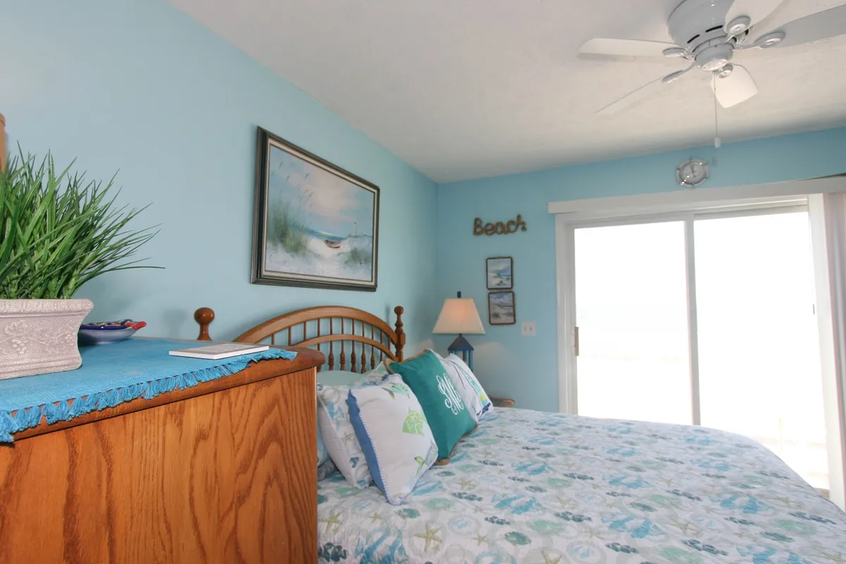 A tranquil bedroom with a bed dressed in colorful bedding, appealing wall art, a nightstand with lamp, and a sliding glass door leading outdoors. The room looks secure, restful, and well-maintained, reinforcing themes of safe, peaceful stays.